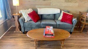 A living room with a grey sofa, red pillows, a wooden coffee table, and a lamp on a side table. - Large Cabin with Stunning View - Fire Pit, Relax & Unwind  (Gallipolis)