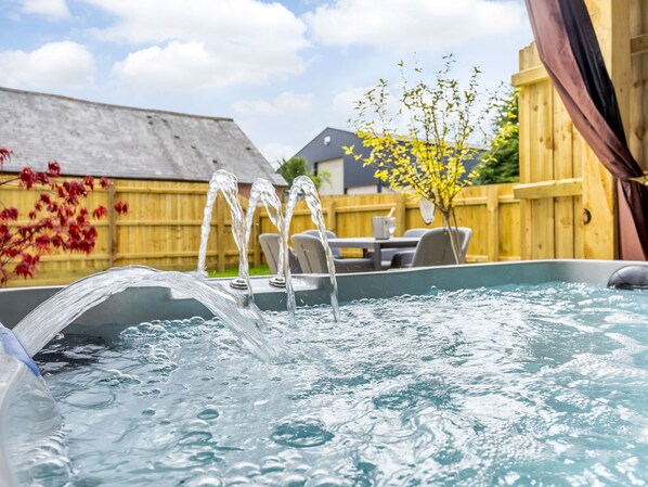 A hot tub with water jets, a wooden fence, and outdoor furniture in the background. - Toppesfield Hall Luxury Cottage With Hot Tub (Halstead)