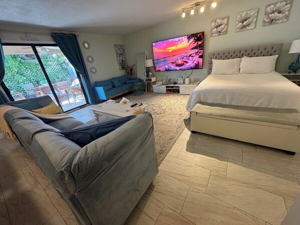 A modern bedroom with a large bed, a sofa, a TV, and a view of the outdoors. - GREAT LOCATION SHORT WALK OR DRIVE TO PLAZAS, CLOSE TO BALL PARKS , BEACHES . (Palm Beach Gardens)