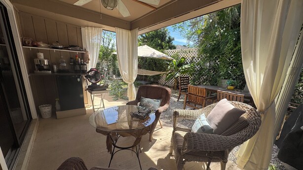 Une terrasse extérieure aménagée avec des meubles en osier, une table en verre et un ventilateur de plafond.