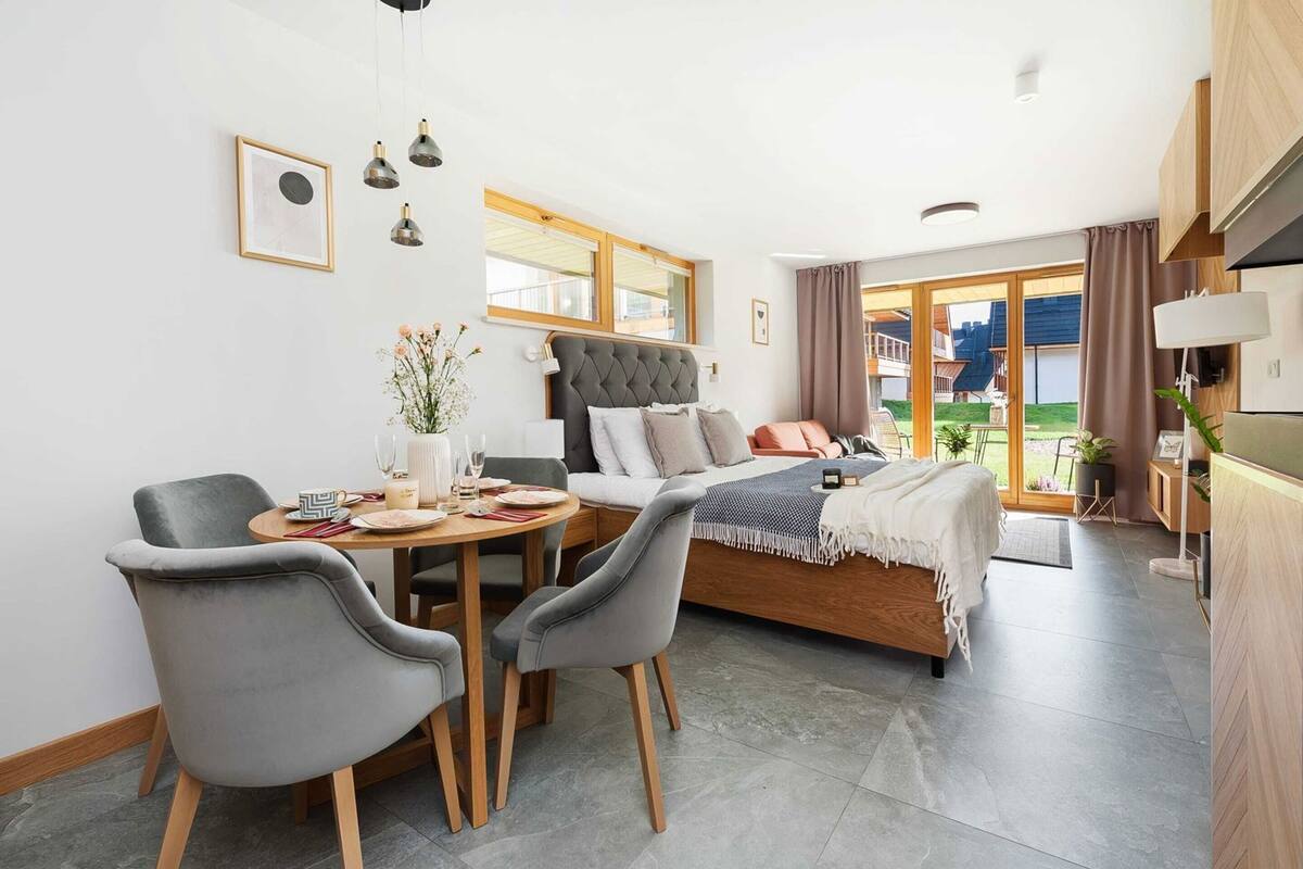 A modern bedroom with a bed, a dining table with chairs, a sofa, and a large window.