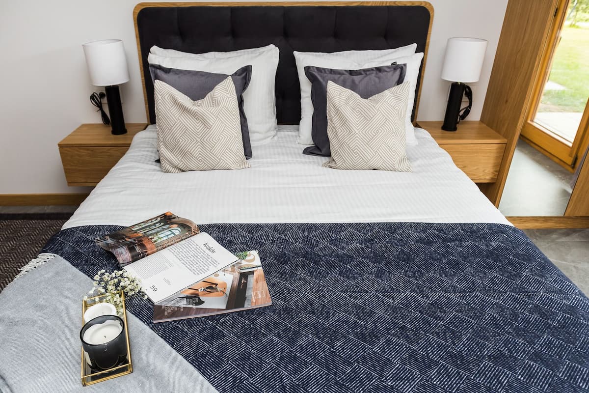 A neatly made bed with a dark blue patterned bedspread, two bedside tables with lamps, and a window with a view of greenery.