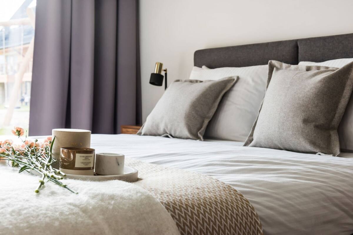 A neatly made bed with pillows, a bedside lamp, and a tray with candles and flowers.