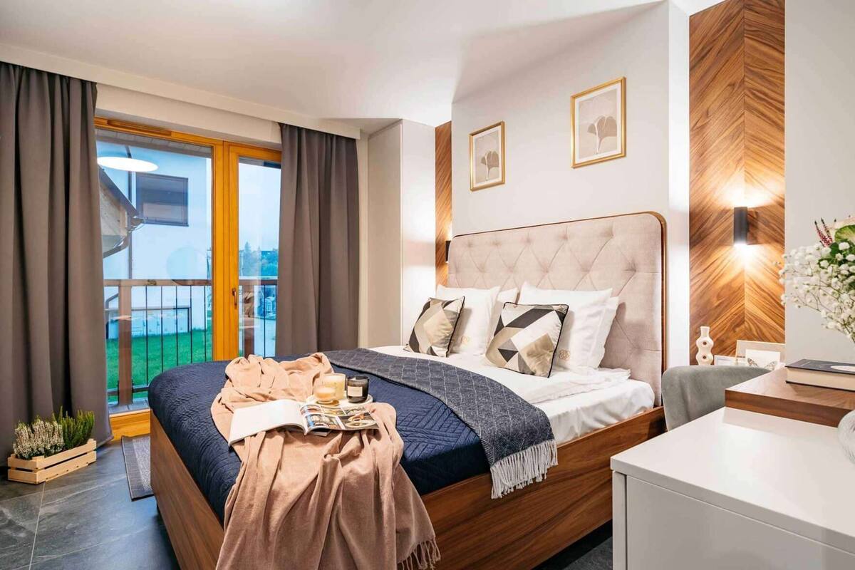 A bedroom with a bed, bedside table, and a view of the outdoors.
