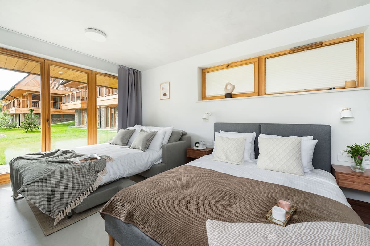 A modern hotel room with two beds, a large window, and a view of the outdoor area.
