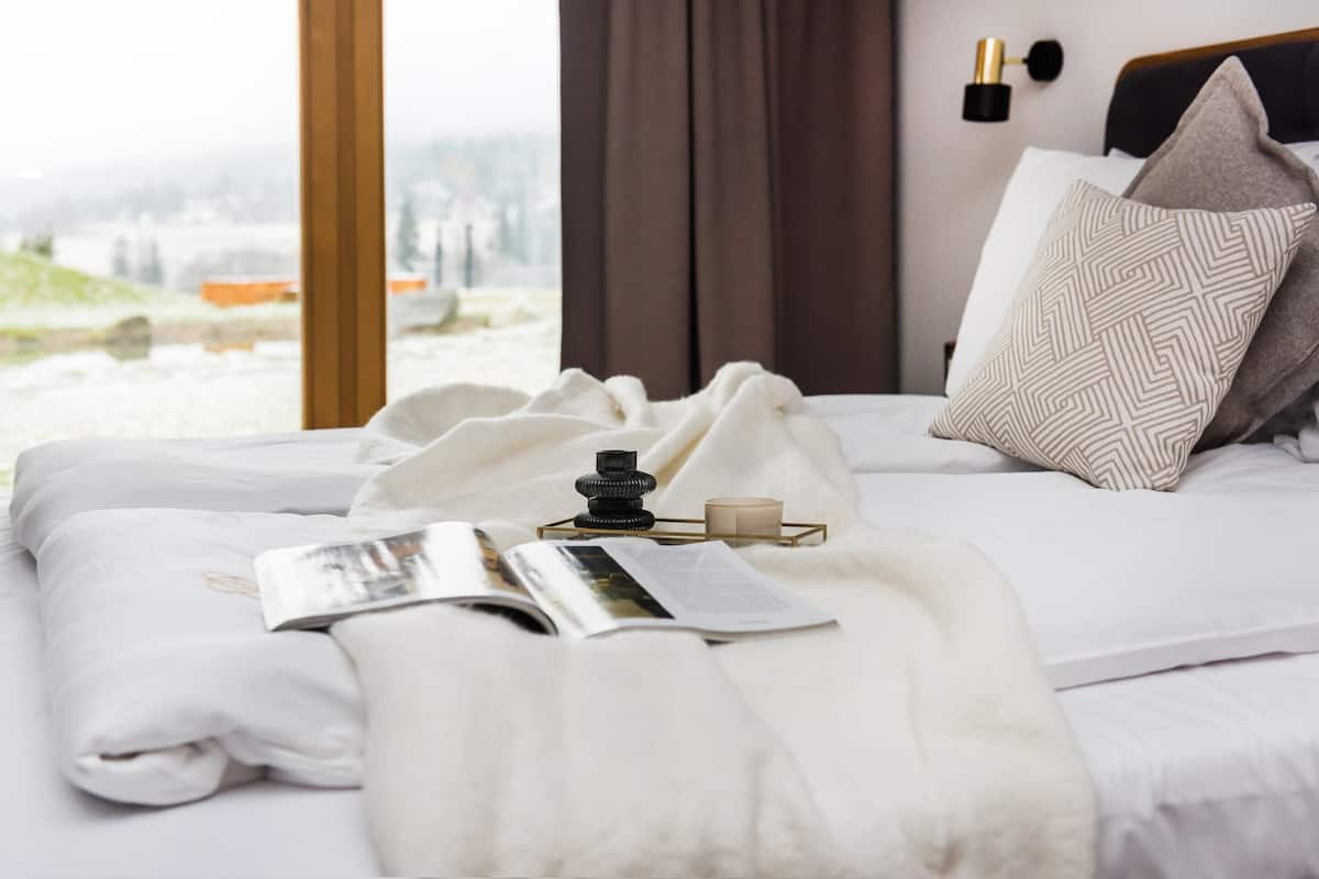 A neatly made bed with a book, a candle, and a decorative item on the bedside table.