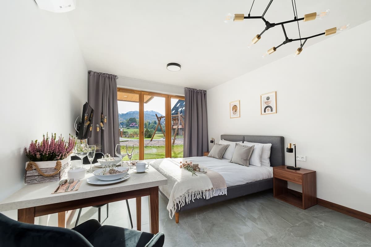 A modern bedroom with a bed, bedside table, and a view of the outdoors.