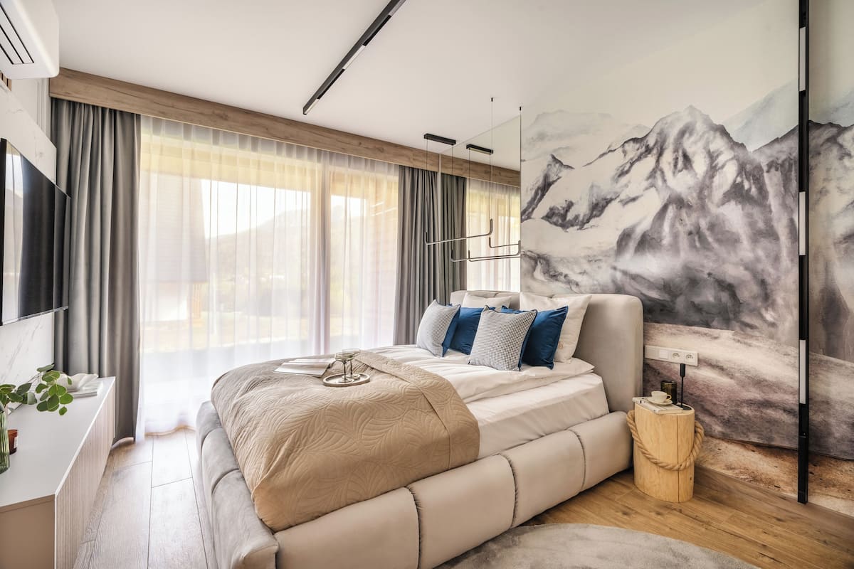 A modern bedroom with a large bed, a desk, and a painting of mountains.