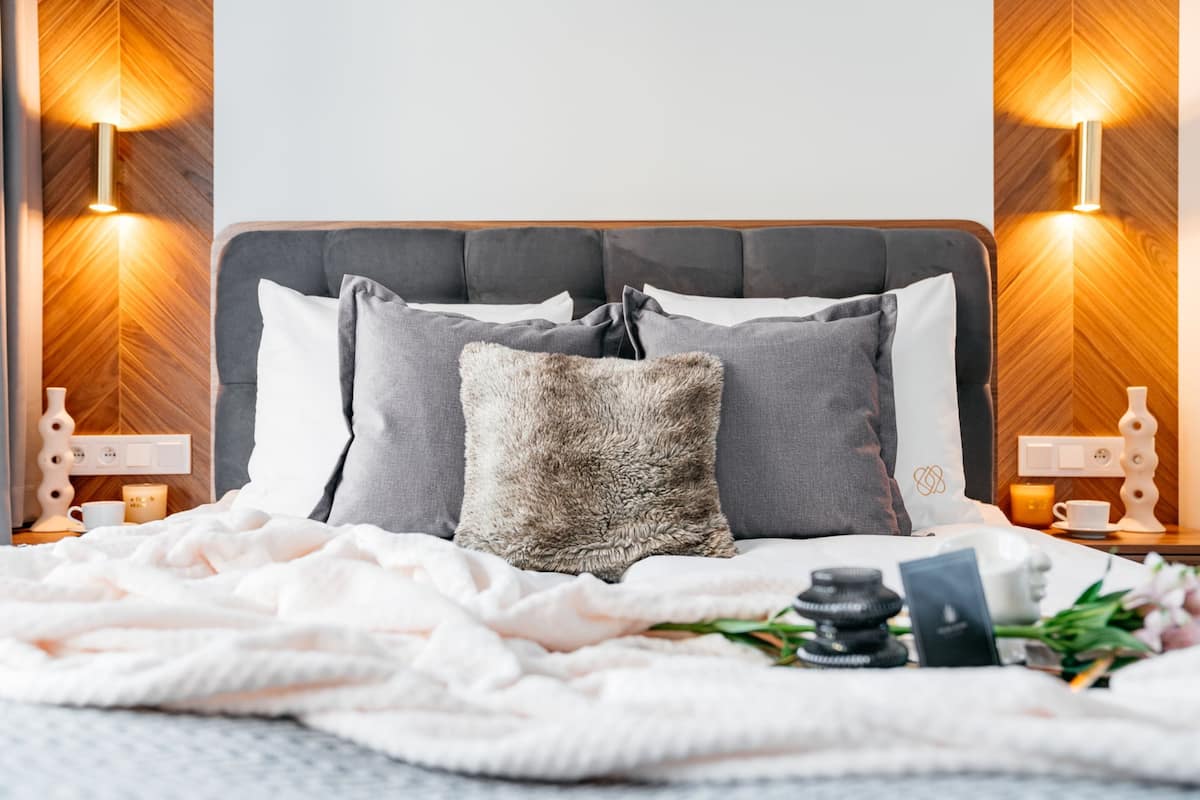 A neatly made bed with a grey headboard, two bedside lamps, and a fluffy pillow.