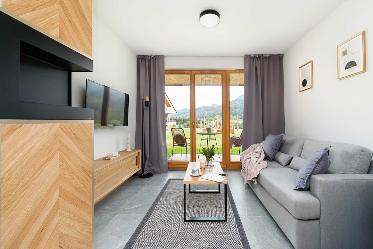 A modern living room with a grey sofa, a coffee table, and a TV mounted on the wall.