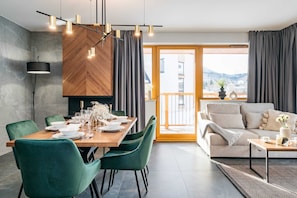 A modern dining area with a wooden table set for four, green upholstered chairs, and a contemporary pendant light fixture. - Polana Resort By Loft Affair (Koscielisko)