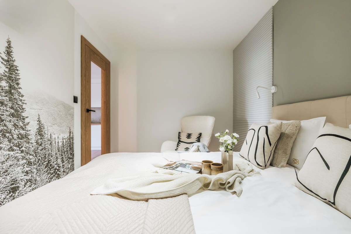 A bedroom with a large bed, a chair, and a wall with a forest mural.