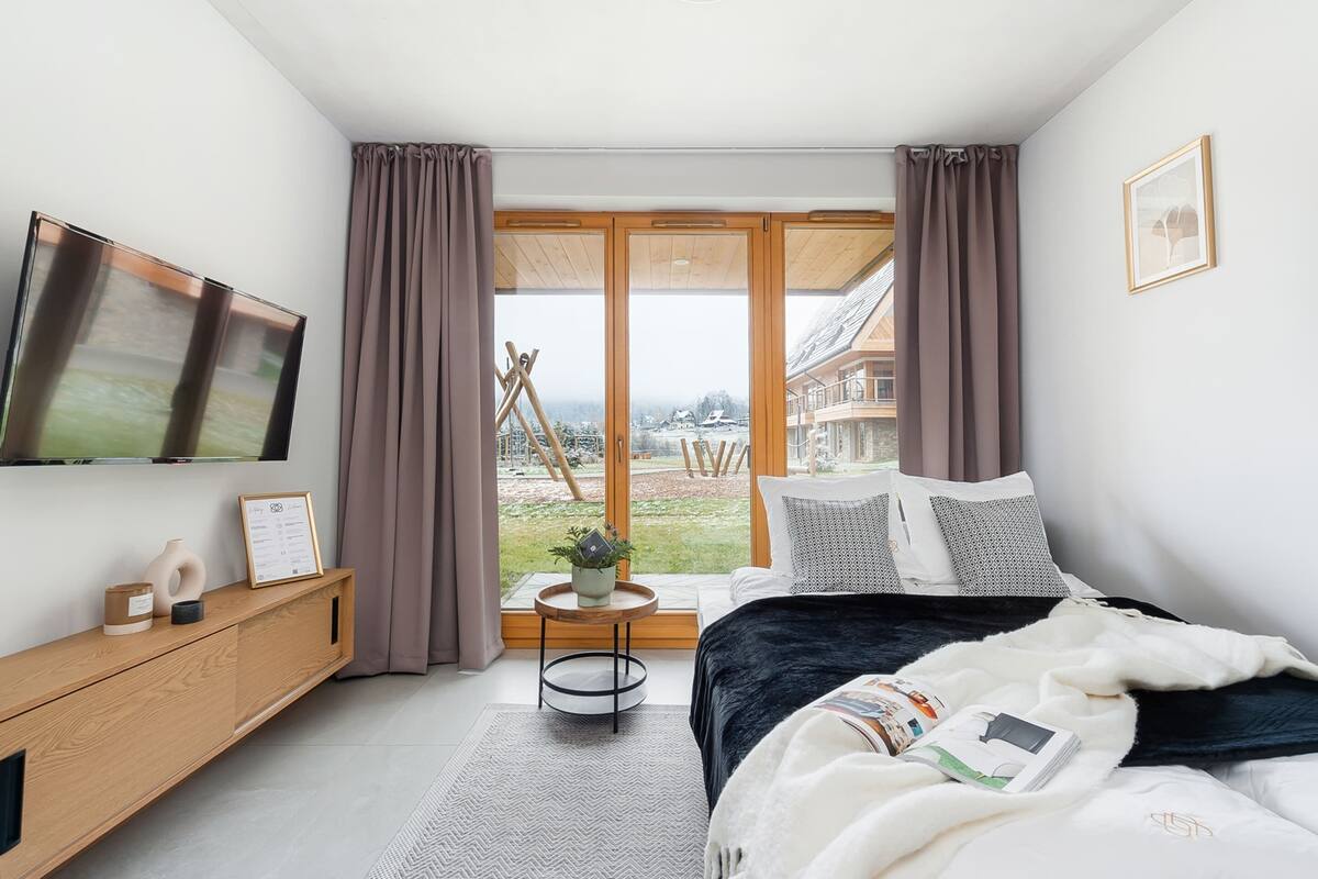 A modern bedroom with a bed, bedside table, TV, and a view of the outdoors.