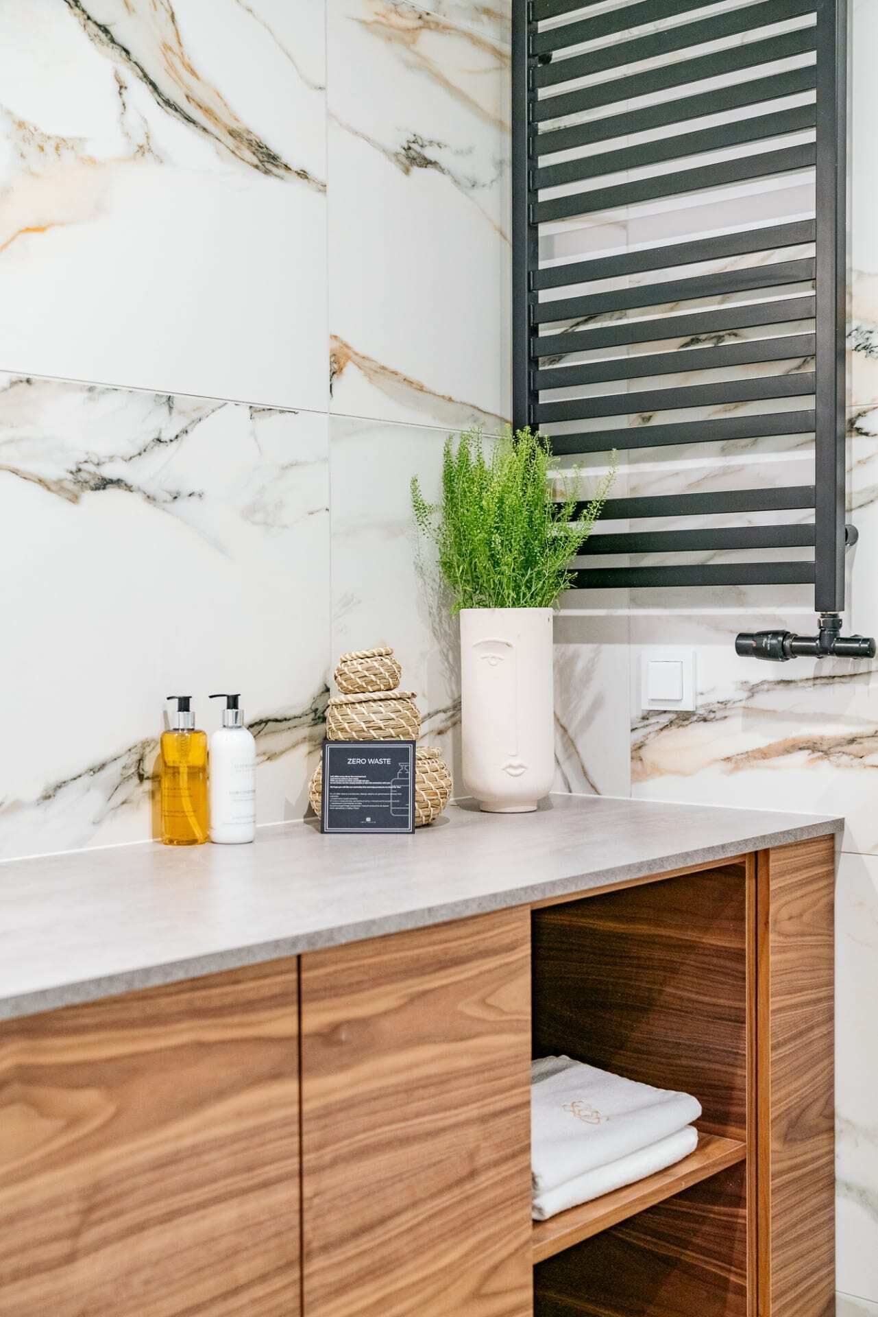 A bathroom vanity with a marble backsplash, a potted plant, and toiletries.