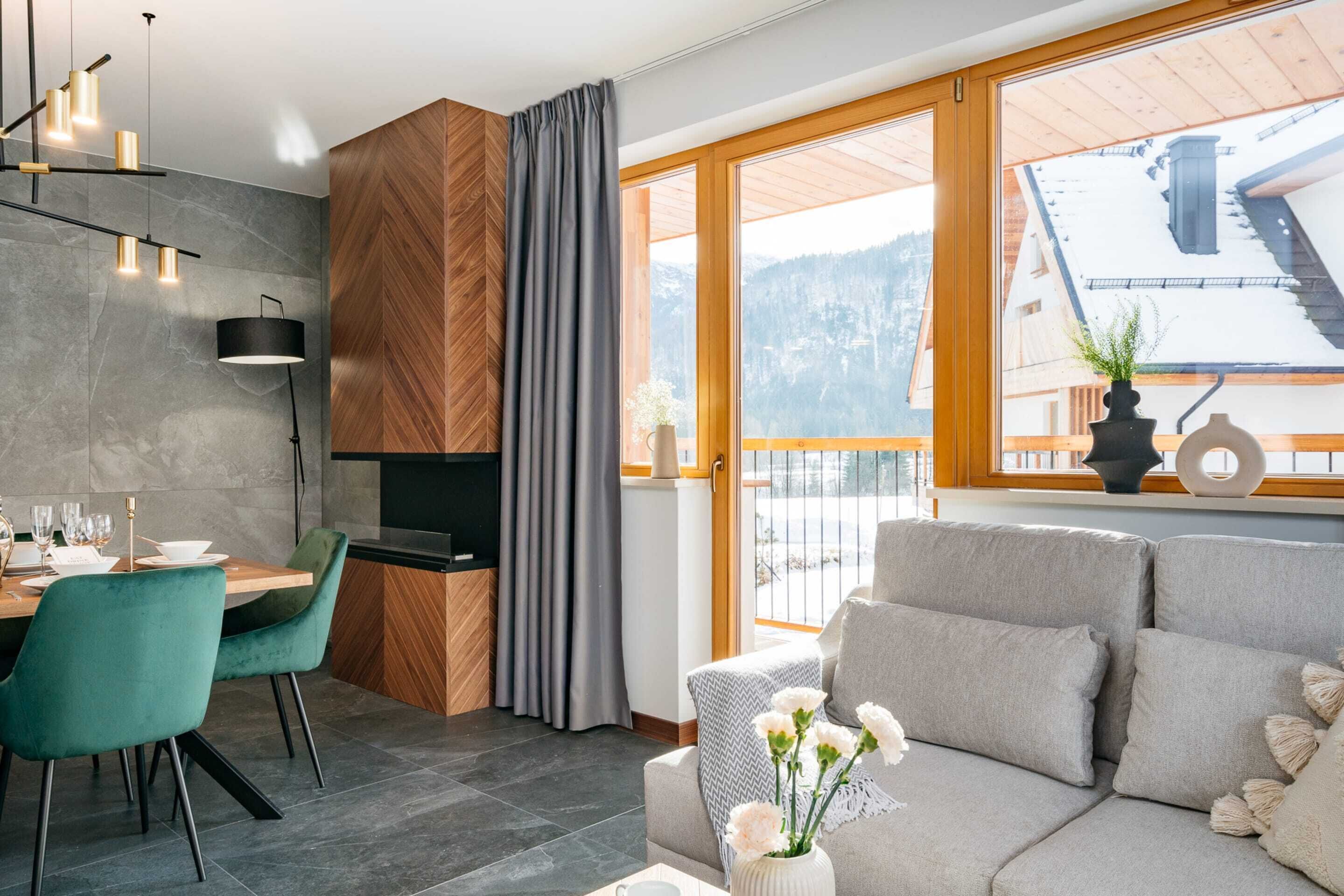 Un salon moderne avec un canapé, une table à manger et des chaises. Une grande fenêtre offre une vue sur les montagnes.