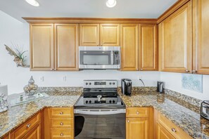 A kitchen with wooden cabinets, a stainless steel microwave, a gas stove, granite countertops, and a coffee maker.