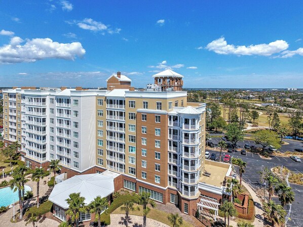 A multi-story hotel with a pool, a tennis court, and a view of the surrounding area.
