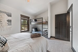 Une chambre avec un lit superposé, un grand lit, une fenêtre et une porte.