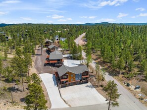 Une grande cabane en rondins à plusieurs étages, dotée d’une allée spacieuse et offrant une vue sur une zone boisée.