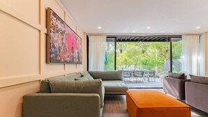 Een moderne woonkamer met een hoekbank, een oranje poef en een groot abstract schilderij aan de muur.