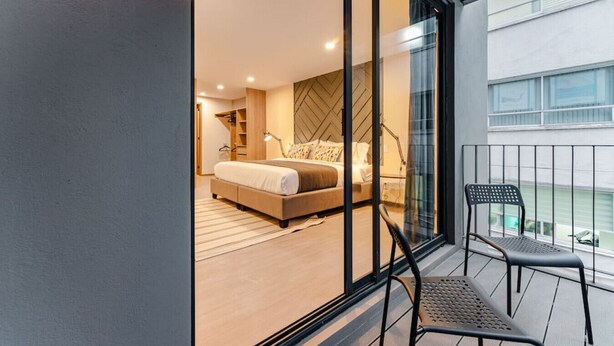 Quarto moderno com uma cama grande, um closet espaçoso e uma varanda com uma cadeira.