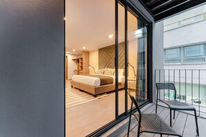 Ein modernes Schlafzimmer mit einem großen Bett, einem begehbaren Kleiderschrank und einem Balkon mit einem Sessel.