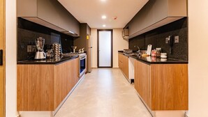 Een moderne keuken met houten kastjes, een zwart aanrecht, een inbouwoven en een blender.