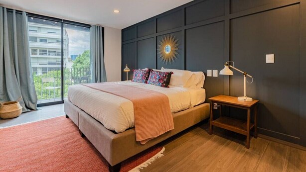 Een moderne slaapkamer met een groot bed, een nachtkastje, een lamp en uitzicht op groen buiten het raam.
