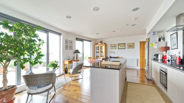 A modern kitchen with a central island, wooden flooring, and a large window providing natural light. - Putney Rooftops (London)