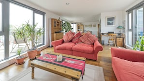 A spacious living area with a red sofa, a wooden coffee table, and potted plants. - Putney Rooftops (London)