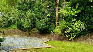 Un camí de pedra delimitat per pals de fusta que serpenteja per una zona enjardinada, amb un fons de vegetació verda i abundant.