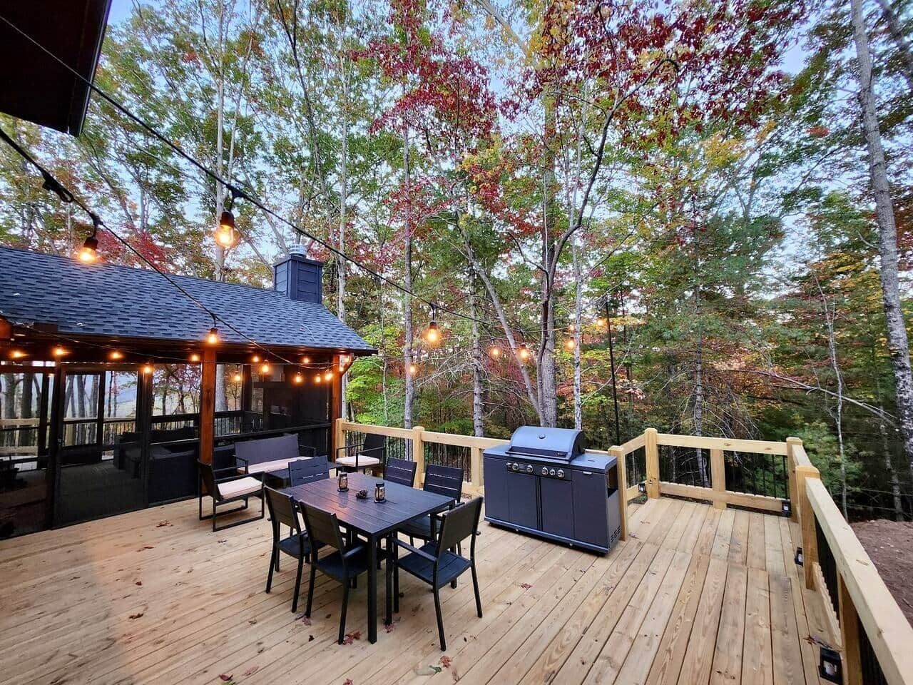 A wooden deck with outdoor furniture, a grill, and string lights.