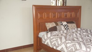 A bed with a wooden headboard, patterned bedding, and two decorative pillows. - MiGo House (Arusha)