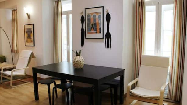 Un comedor con una mesa negra, cuatro sillas, un centro de mesa con piña y un cuadro en la pared.