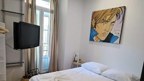 Una habitación de hotel con una cama, un televisor fijado a la pared y un cuadro sobre la cama.