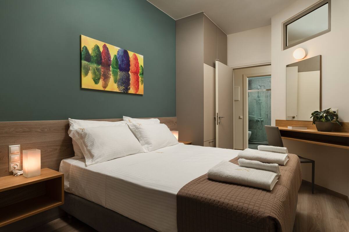 A modern hotel room with a bed, bedside table, and a painting on the wall.