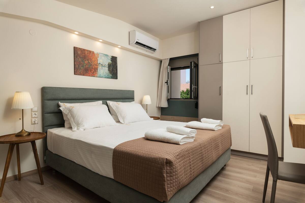 A neatly made bed with a brown quilt, two bedside lamps, a painting on the wall, and a wardrobe with sliding doors.