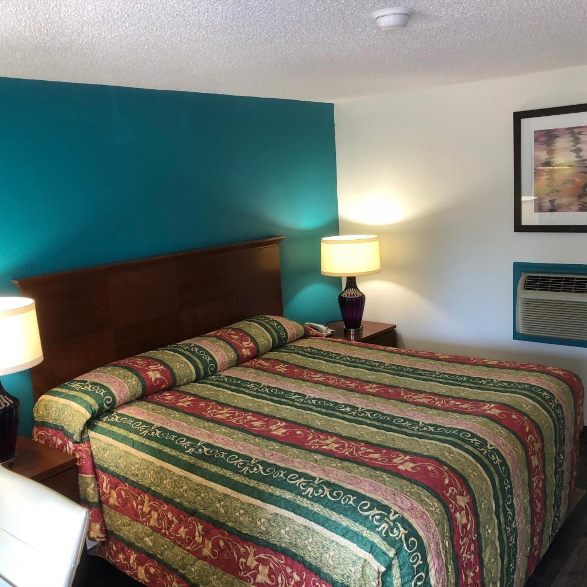 A hotel room with a bed, a nightstand, a lamp, and a wall-mounted air conditioner.