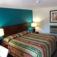 A hotel room with a bed, a nightstand, a lamp, and a wall-mounted air conditioner.