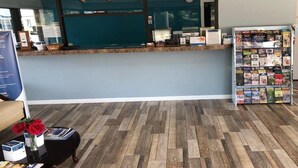 Zona de recepción con suelo de madera, mostrador de recepción, ordenador y un atril con revistas.