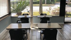 Interior de restaurante con mesas y sillas, vista de la calle y una planta en maceta.