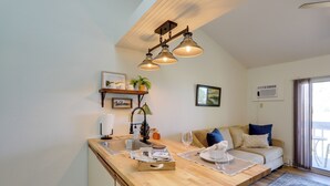 Una cocina moderna con encimera de madera, un lavaplatos integrado y una zona de comedor con mesa y sillas. Hay un sofá y una ventana con cortinas en la sala de estar.