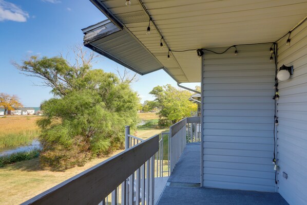 A covered porch with a metal railing, overlooking a grassy area with trees and a body of water.