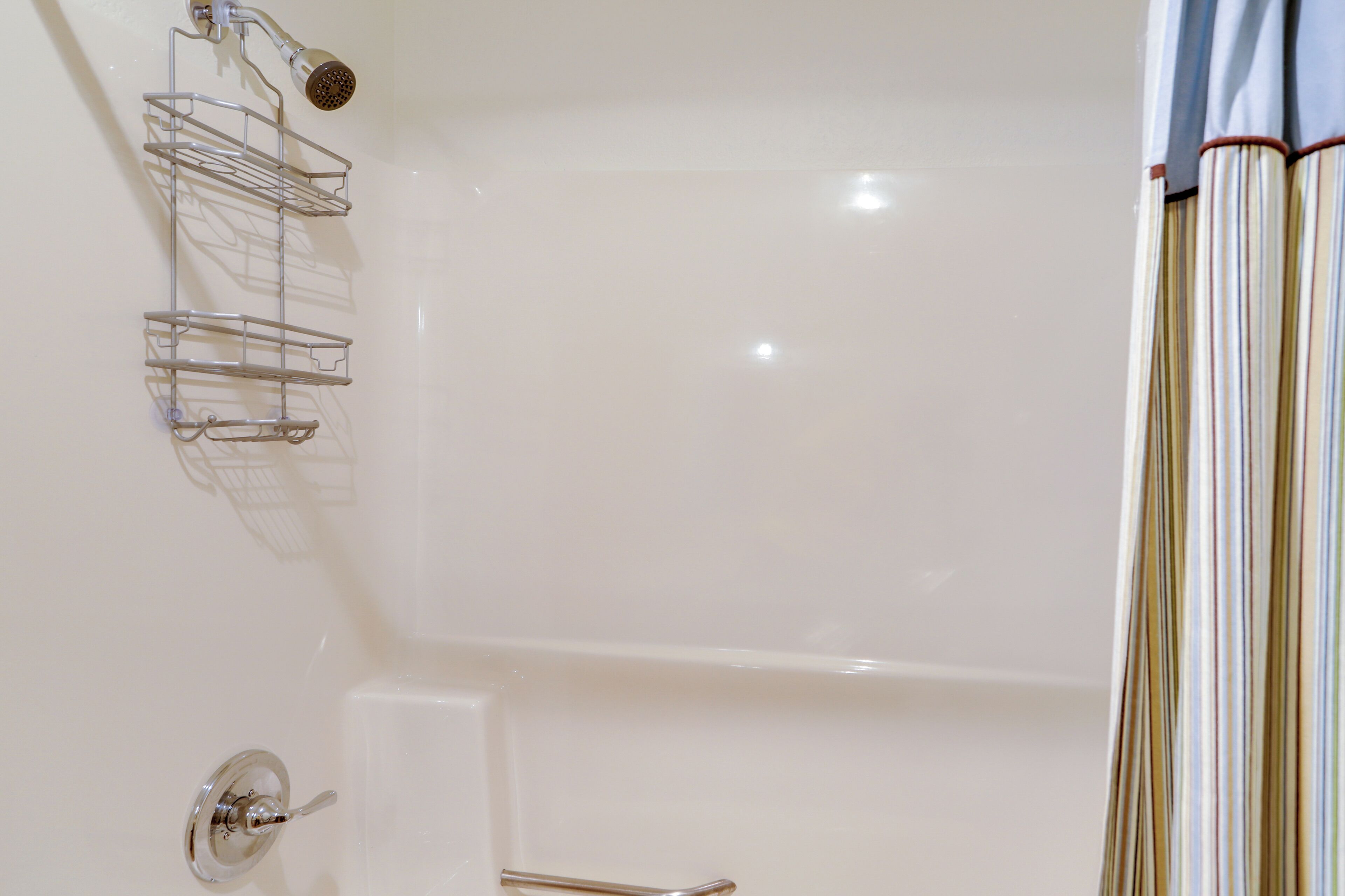 A bathtub with a chrome faucet, a showerhead, and a chrome shelf with a towel.