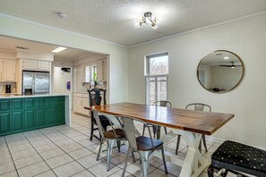 A kitchen with a wooden dining table, chairs, and a bench. There is a refrigerator, cabinets, and a window.