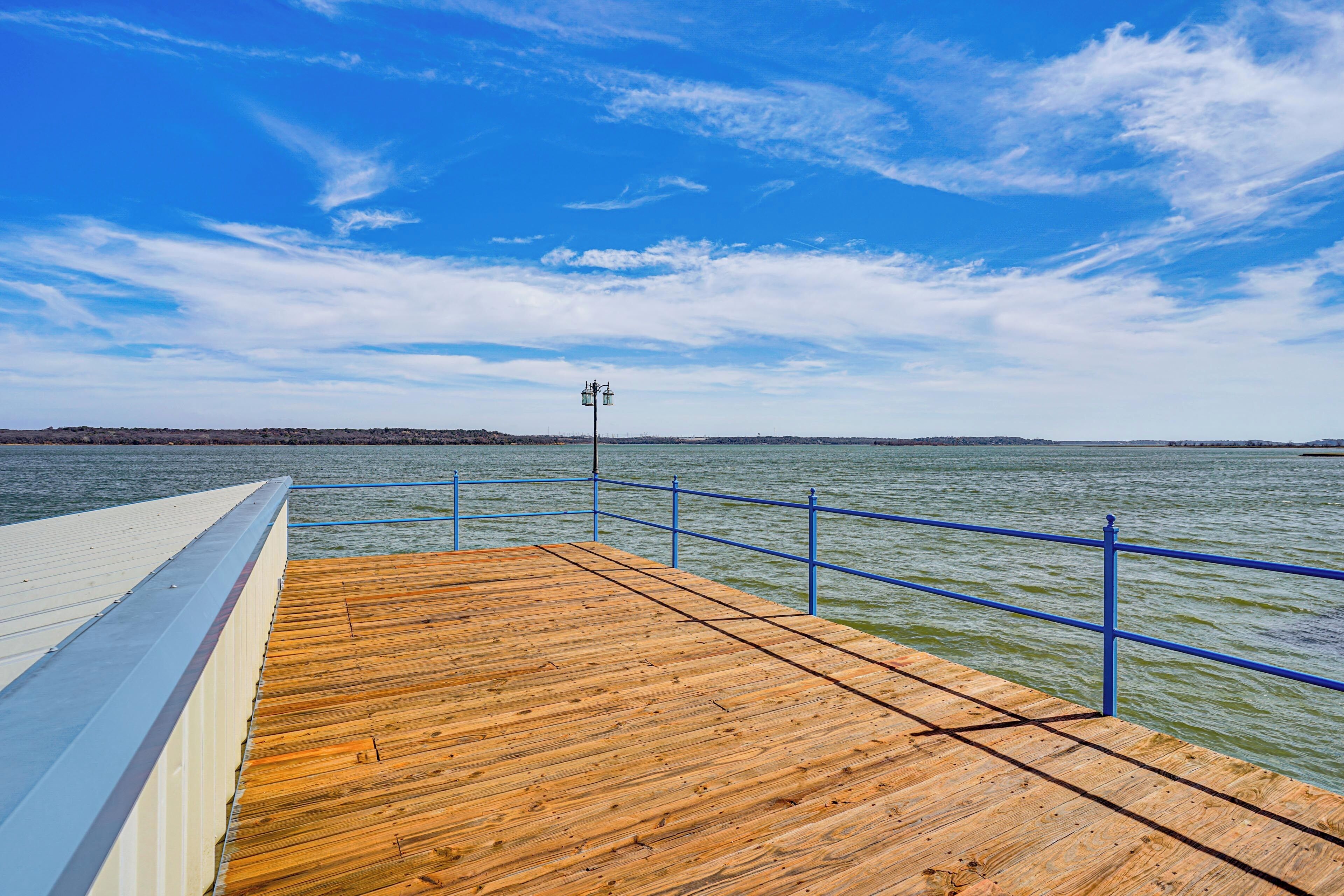 A wooden pier with a blue railing extending over water, under a clear sky.