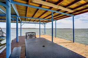 A covered wooden deck with a table and chairs, overlooking a body of water.