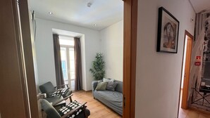A living room with a sofa, a dining table with chairs, a potted plant, and a painting on the wall. - Bairro Alto - 3 bedroom apartment with 2,5 bathrooms (Lisboa)