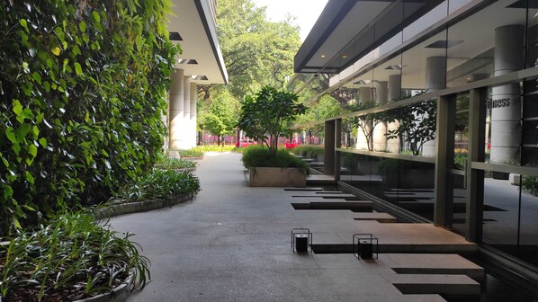 A modern indoor corridor with a glass wall, potted plants, and a central planter.