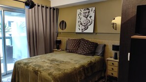 A bedroom with a bed, a nightstand, a lamp, a painting on the wall, and a window with curtains.